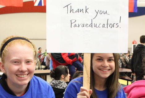 Two students sit while holding a sign that reads "Thank you paraeducators."